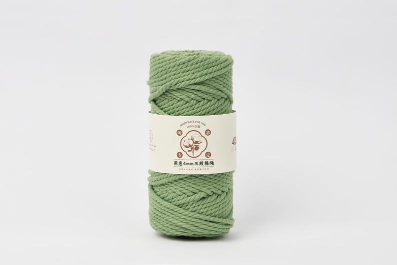 May include: A cylindrical spool of sage green cotton cord wrapped in a cream-colored paper band. The band features a central brown graphic of a cotton plant, Chinese characters, and the text 4mm, indicating the thickness of the twisted cord.