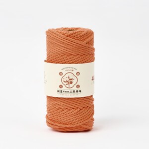 May include: A spool of terracotta-colored twisted cotton cord wrapped in a cream-colored paper label. The label features a central graphic of a cotton boll, the text 4mm, and Chinese characters. The cord has a thick, three-strand twisted texture.