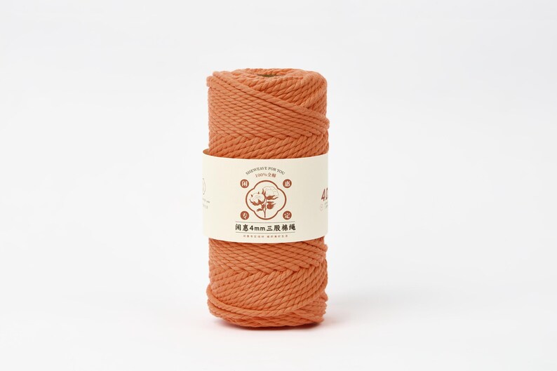 May include: A spool of terracotta-colored twisted cotton cord wrapped in a cream-colored paper label. The label features a central graphic of a cotton boll, the text 4mm, and Chinese characters. The cord has a thick, three-strand twisted texture.