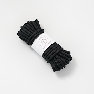 May include: A tightly wound bundle of black macrame cord, wrapped with a white label. The label features text and a small graphic. The cord appears to be approximately 8mm in diameter. The product is suitable for crafting and DIY projects.