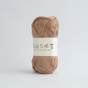 May include: A ball of light brown yarn with a white label wrapped around it. The label has Chinese characters and the text "xue fei er mian cao". The yarn is tightly wound and appears to be made of paper or a similar material.