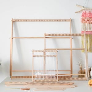 May include: A collection of light-colored wooden weaving looms in various sizes, featuring notched top and bottom bars for tensioning warp threads. The set includes several rectangular frames and flat wooden components arranged on a surface.