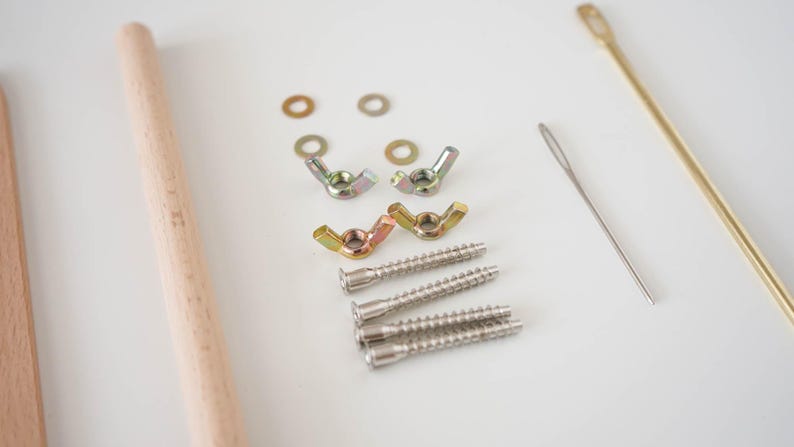 May include: A hardware assembly kit containing two light-colored wooden dowels, four metal washers, four metal wing nuts, four threaded metal screws, one silver-toned sewing needle, and one long, thin, gold-toned metal rod with an eyelet at one end.