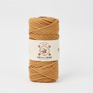 May include: A cylindrical spool of golden-brown twisted cotton cord wrapped in a cream-colored paper label. The label features a central circular graphic of a cotton plant, Chinese characters, and the text 4mm, indicating the cord thickness.