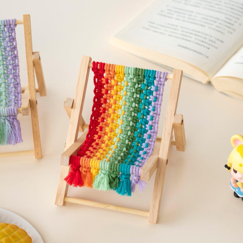 May include: Miniature wooden deck chair with a rainbow-colored macrame seat and matching tassels. The chair has a natural wood frame and is designed for decorative purposes. The colorful design adds a playful touch to any space.