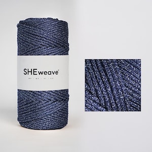 May include: A cylindrical spool of dark blue cord with a metallic shimmer, wrapped in a white paper band featuring the black text SHEweave. The cord has a braided texture, and a square inset shows a detailed view of the dark blue metallic fibres.