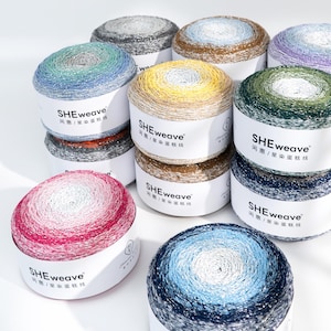 May include: A collection of colorful yarn skeins in various shades, including blue, green, yellow, and pink. Each skein is labeled with the text "SHEweave" and Chinese characters. The yarn appears to be a gradient color, with a metallic sheen.