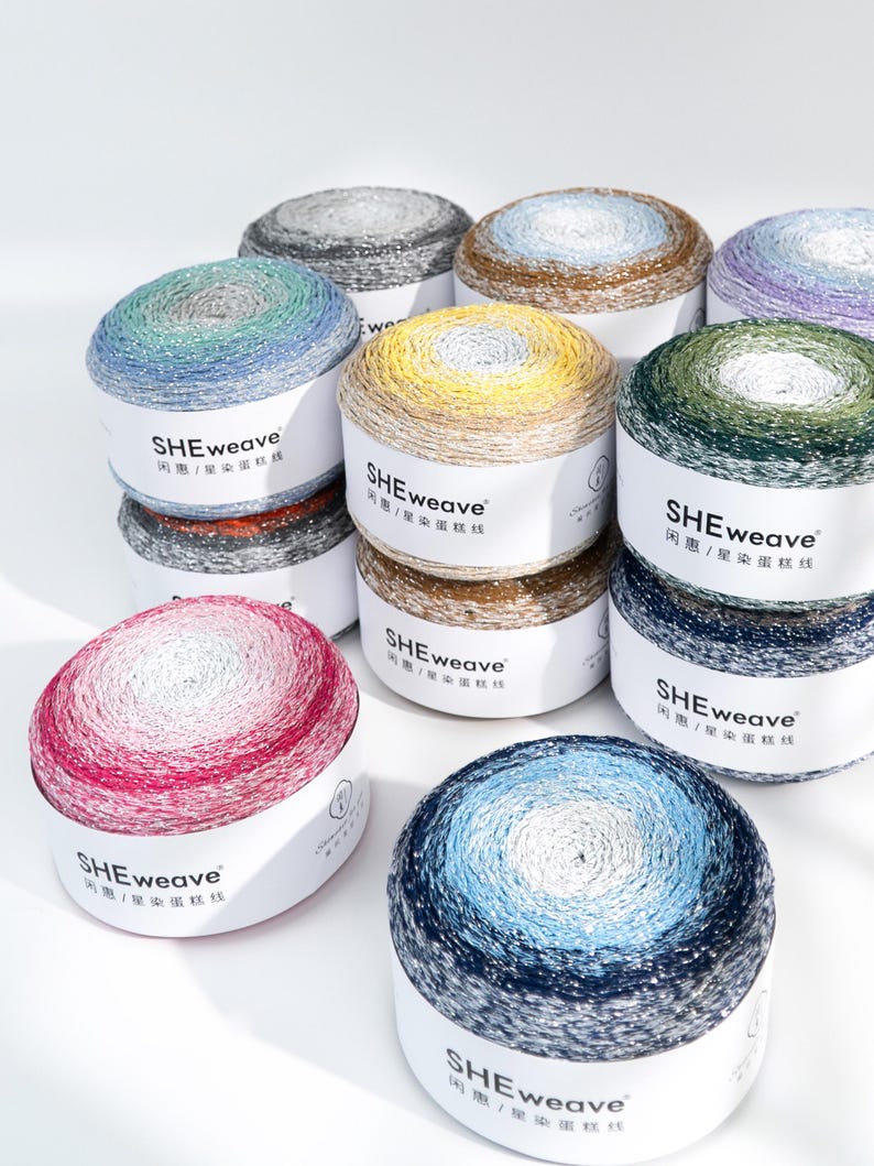 May include: A collection of colorful yarn skeins in various shades, including blue, green, yellow, and pink. Each skein is labeled with the text "SHEweave" and Chinese characters. The yarn appears to be a gradient color, with a metallic sheen.