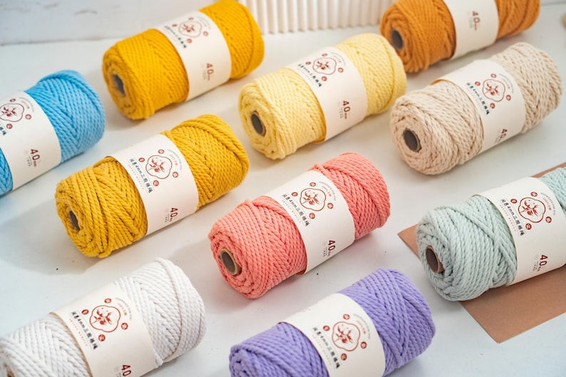 May include: A collection of ten spools of twisted cotton cord in various colors including yellow, blue, pink, purple, cream, and orange. Each spool features a white paper band with a circular logo and the text 4.0mm printed on the front.