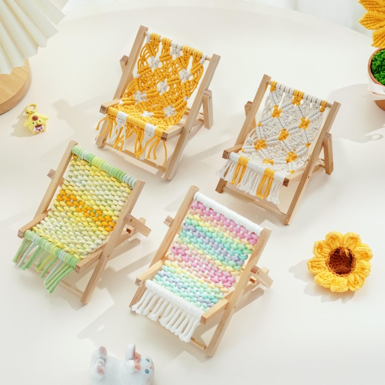 May include: Four miniature wooden deck chairs with woven seats in various colors: yellow, white, green, and rainbow. Each chair has a fringe detail at the bottom. A yellow crocheted sunflower is also present.
