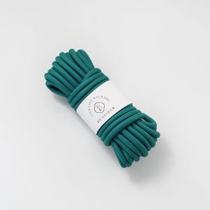 May include: A bundle of teal macrame cord wrapped with a white label. The label has the text "SILK WEAVE MACRAME" and other text in a different language. The cord appears to be 8mm in diameter.