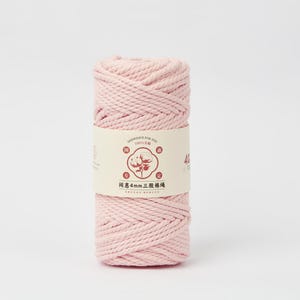 May include: A cylindrical spool of light pink cotton cord wrapped in a paper band. The band features a central circular graphic of a cotton plant, Chinese characters, and the text 4mm, indicating the thickness of the twisted fiber material.
