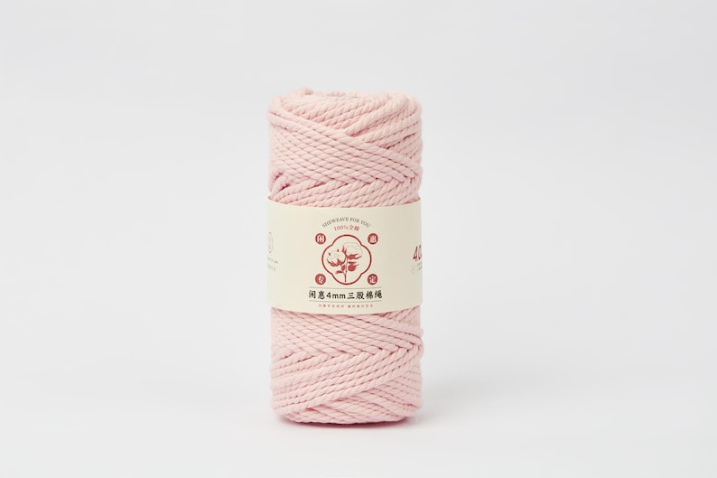 May include: A cylindrical spool of light pink cotton cord wrapped in a paper band. The band features a central circular graphic of a cotton plant, Chinese characters, and the text 4mm, indicating the thickness of the twisted fiber material.