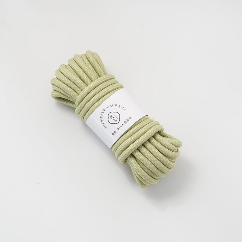 May include: A bundle of light green macrame cord, wrapped with a white label. The label features the text "SHEWEAVE MACRAME" and other text in a foreign language. The cord appears to be approximately 8mm in diameter.
