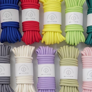 May include: A collection of fifteen bundles of macrame cord in various solid colors including black, pink, blue, red, yellow, lime green, teal, light blue, beige, gray, white, lavender, olive green, soft pink, and turquoise, each with a white label.