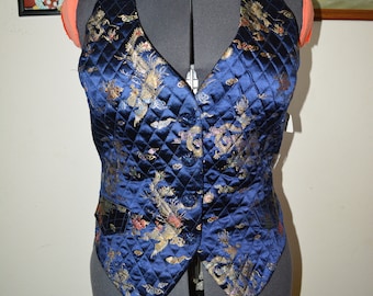 May include: A blue quilted vest with a gold and floral pattern. The vest has a V-neck and a button closure.