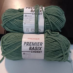 May include: Two skeins of green Premier Basix Chunky yarn. Each skein has a label with the text "Premier Basix Chunky", "Bulky", and measurements of 107 m and 100 g. The yarn is 100% Acrylic.