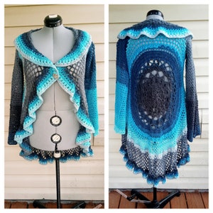 May include: A crocheted cardigan with a blue, teal, and gray color gradient. The cardigan has a ruffled hem and a large, openwork design on the back.