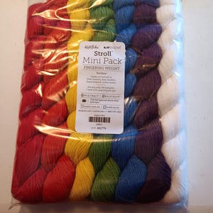 Può includere: Una busta di plastica trasparente contenente un mini pacco di filato arcobaleno. Il filato è disposto in un gradiente di rosso, arancione, giallo, verde, blu, viola e bianco. L'etichetta recita "Stroll Mini Pack Fingering Weight Rainbow".