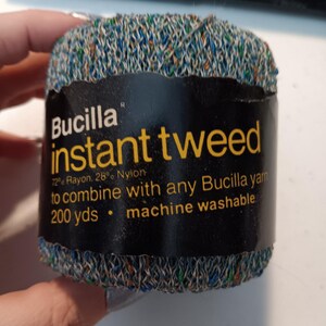 May include: A ball of Bucilla instant tweed yarn featuring a blue, green, and orange speckled texture. The black label displays the text: Bucilla instant tweed, 72% Rayon, 28% Nylon, to combine with any Bucilla yarn, 200 yds, machine washable.