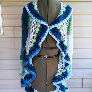 May include: A crocheted cardigan with a ruffled hem in shades of blue, green, and white. The cardigan is open in the front and has a V-neck.