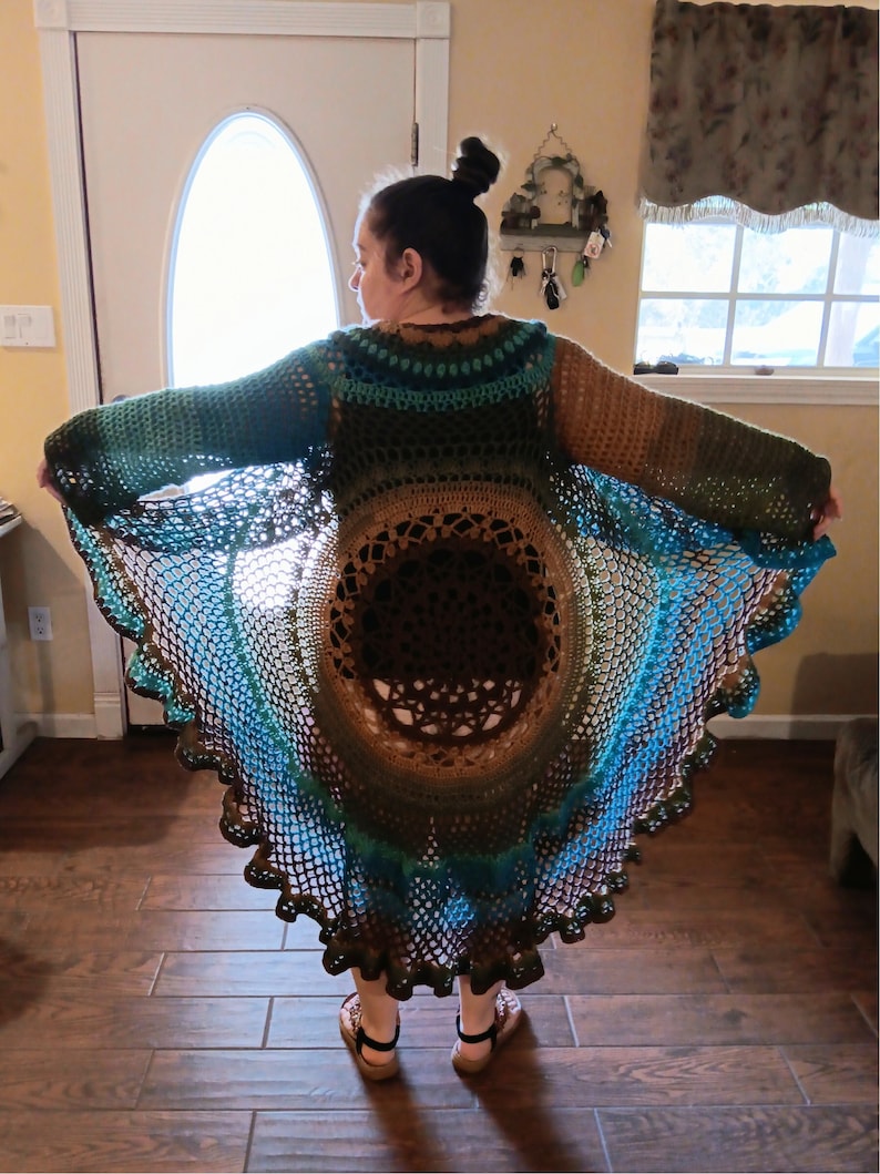 May include: A crocheted cardigan with a circular design in shades of brown, green, and blue. The cardigan has a scalloped hem and is open in the front.