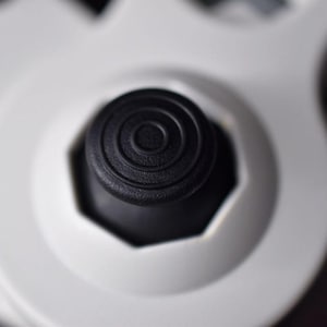 May include: Close-up of a black circular button with concentric circles on a white gaming controller.