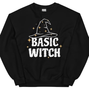 以下が含まれることがあります： 白い魔女の帽子と「BASIC WITCH」の文字がプリントされた黒いスウェットシャツ。魔女の帽子には金の星のアクセントが付いています。ハロウィンや普段使いにぴったりのカジュアルなトップスです。