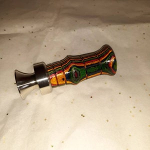 May include: A handcrafted bottle stopper with a stainless steel base and a colorful, layered wood handle. The handle features bands of red, green, yellow, and blue. The stopper is designed to fit into a bottle opening.