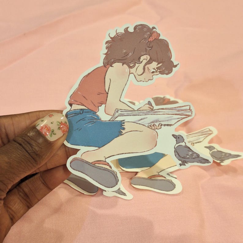 Op de afbeelding: Een sticker met een cartoonillustratie van een persoon die in een notitieboek schrijft, een rode top en een blauwe korte broek draagt. Er zijn ook twee kraaien afgebeeld. De sticker staat op een roze achtergrond.