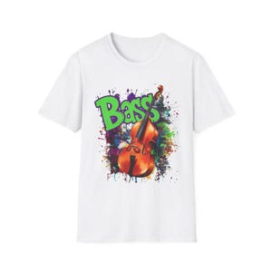 Puede incluir: Camiseta blanca con un gráfico de un contrabajo y la palabra "Bass" en verde. El diseño incluye salpicaduras de pintura en varios colores, creando un aspecto vibrante y artístico. Un artículo de ropa con temática musical.