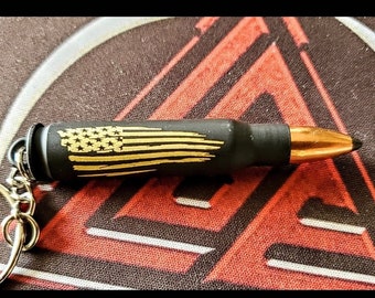 May include: A black and gold bullet keychain with an American flag design. The bullet is attached to a silver key ring.