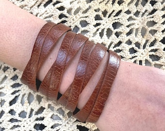 May include: A brown leather cuff bracelet with a woven design. The bracelet is made of multiple strips of leather that are woven together to create a unique and stylish look.