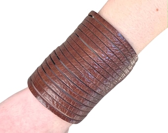 Könnte beinhalten: Ein braunes Lederarmband mit mehreren Lederschichten. Das Armband wird am Handgelenk getragen.
