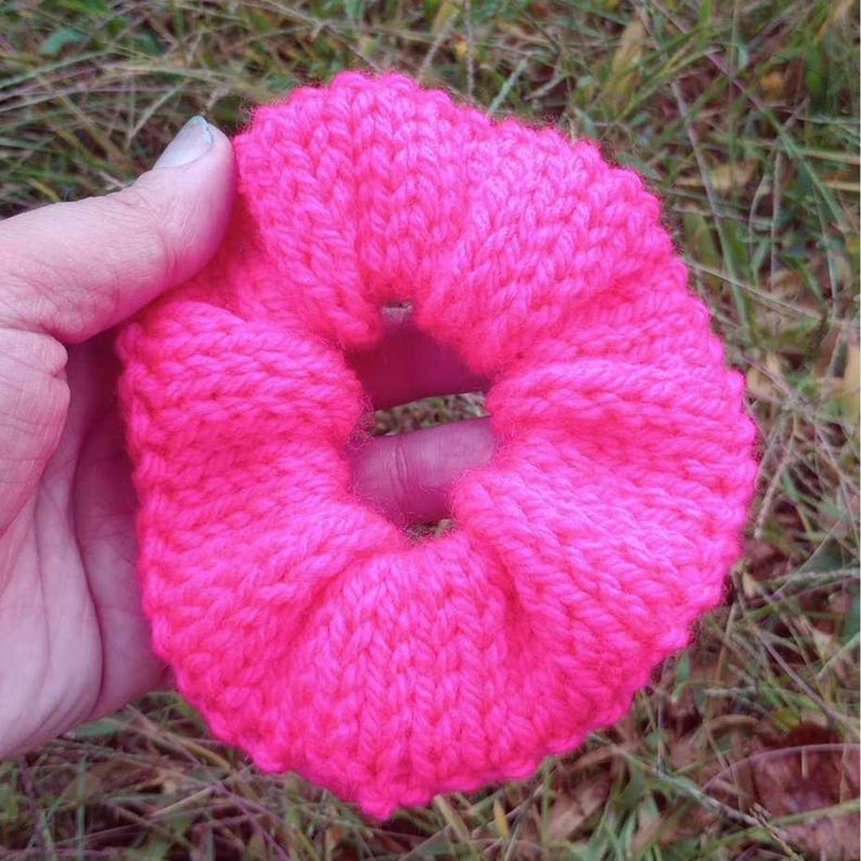 May include: A bright pink knitted hair scrunchie. The scrunchie is made of a soft, fluffy yarn and has a simple, classic design.