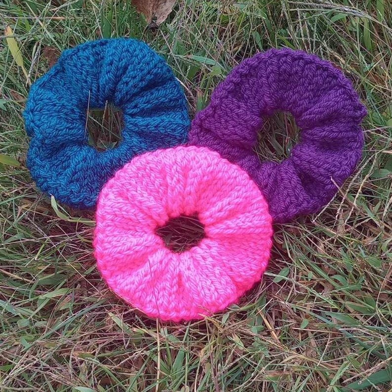 May include: Three crocheted hair scrunchies in different colors: teal, purple, and pink.