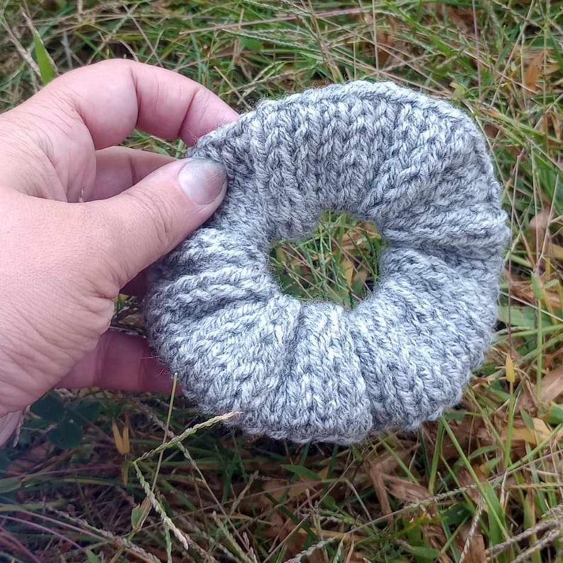 Pu&ograve; includere: Un elastico per capelli a forma di ciambella, lavorato a maglia in grigio e bianco.