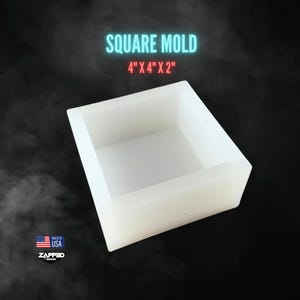 May include: A white square mold with the text "SQUARE MOLD 4" X 4" X 2"" in blue and red. The mold is made in the USA by ZAPPED Design. The mold is 4 inches by 4 inches by 2 inches.