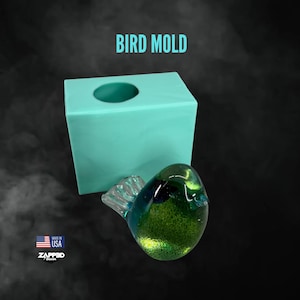 May include: A teal-colored bird mold with a round opening, next to a glass bird figurine. The figurine is green and blue with a clear tail. The text "BIRD MOLD" is at the top. The image also includes a "Made in USA" logo.