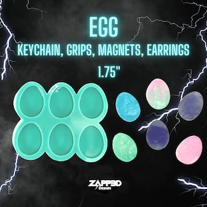 May include: A teal silicone mold with eight egg-shaped cavities.  The mold is used to create resin eggs for keychains, grips, magnets, and earrings.  The text "EGG KEYCHAIN, GRIPS, MAGNETS, EARRINGS 1.75" is displayed above the mold.  There are six resin eggs in various colors, including pink, blue, and green.