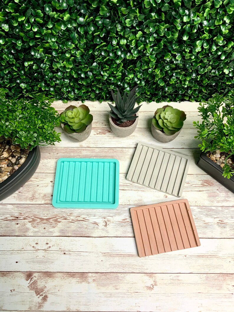 Puede incluir: Tres posavasos cuadrados de hormig&oacute;n con un dise&ntilde;o acanalado. Los posavasos son de color turquesa, gris y marr&oacute;n claro. Los posavasos est&aacute;n sobre una superficie de madera blanca.