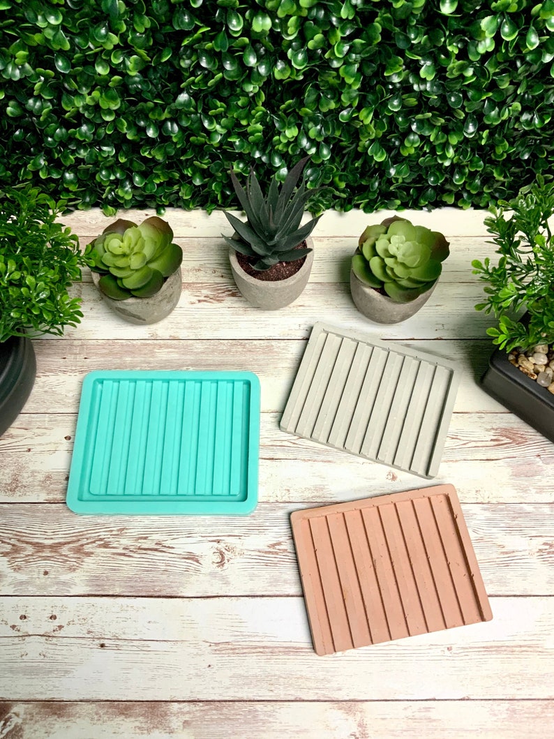Puede incluir: Tres moldes de silicona cuadrados para hacer posavasos de hormig&oacute;n. Los moldes son de color turquesa, gris y marr&oacute;n. Los moldes tienen una textura acanalada.