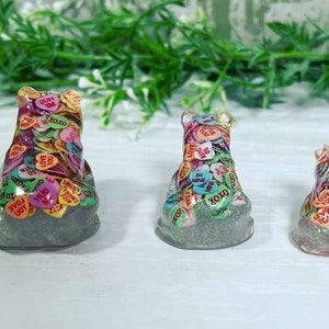 Może przedstawiać: Trzy figurki niedźwiedzi z żywicy, każda pokryta kolorowymi serduszkami z cukierk&oacute;w z napisami takimi jak "Love You", "XOXO" i "Hug Me".