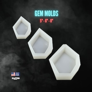 May include: Three white silicone molds for making resin gems. The molds are shaped like a hexagon with a rounded top. The molds are 5 inches, 6 inches, and 8 inches in size. The text "GEM MOLDS" and "5" - 6" - 8" is printed in white on a black background.