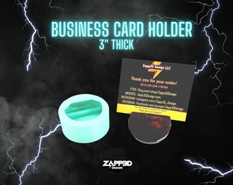 May include: A light blue business card holder made of resin. The holder is 3 inches thick and has a slot for a business card. The holder is on a black background with lightning bolts.
