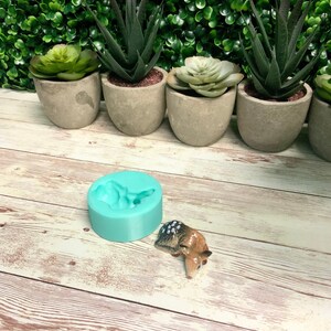 May include: A turquoise silicone mold shaped like a deer, with a small ceramic deer figurine next to it. The mold is on a light wood surface.