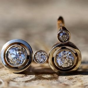 Könnte beinhalten: Ein goldener Ring mit drei runden Diamanten, die in einem kreisförmigen Design gefasst sind. Die Diamanten haben unterschiedliche Größen und sind in einem abgestuften Muster gefasst.