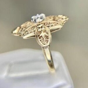 May include: A gold-toned ring with an ornate, filigree design. The ring features a central, clear gemstone and intricate detailing on the band and setting. The ring's design is reminiscent of vintage or antique jewelry.