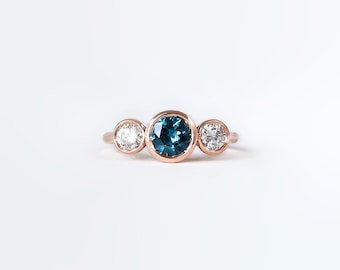 May include: A three-stone ring with a bezel-set blue sapphire and two bezel-set round diamonds.