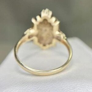 May include: A gold ring with an oval-shaped centerpiece. The ring's band is a simple, polished gold. The centerpiece has a detailed, ornate design, possibly with a gemstone setting. The ring is likely a piece of jewelry.